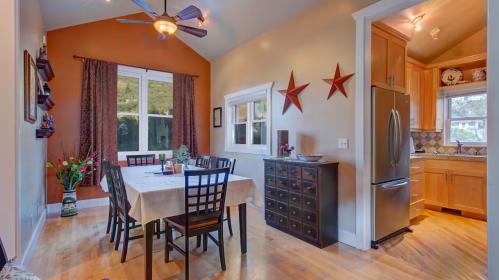 A cozy dining area with a wooden table, chairs, and a view of a kitchen, featuring warm colors and decorative stars.